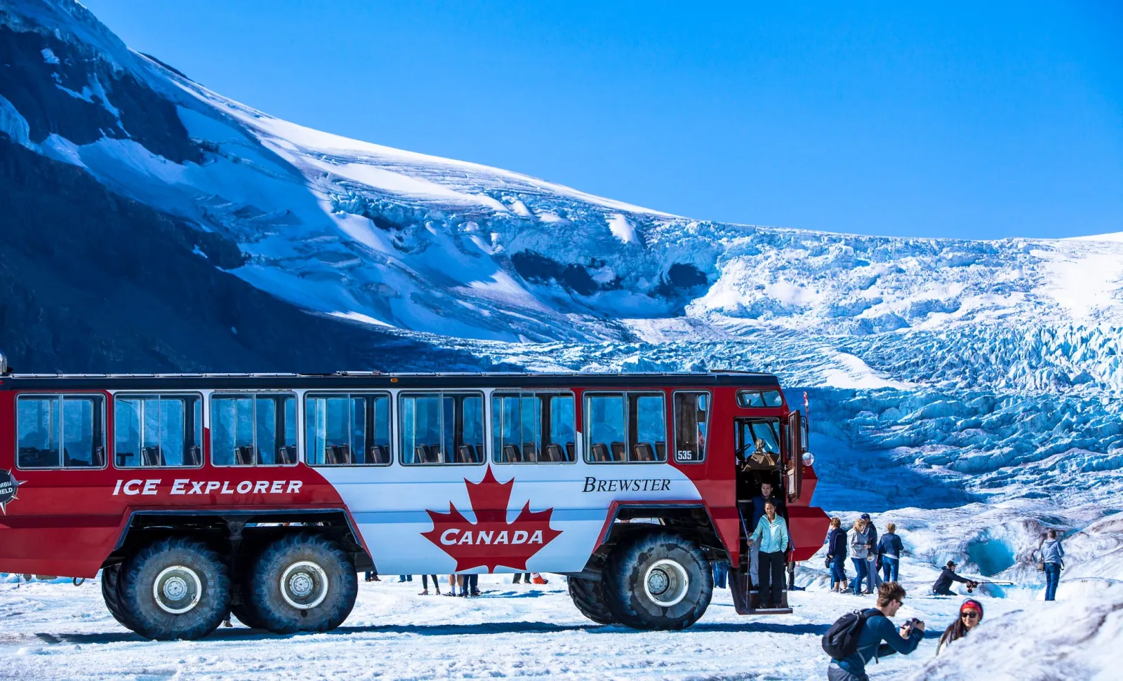 A red Ice Explorer parked on the Athabasca Glacier with the crevassed icefall rising behind it