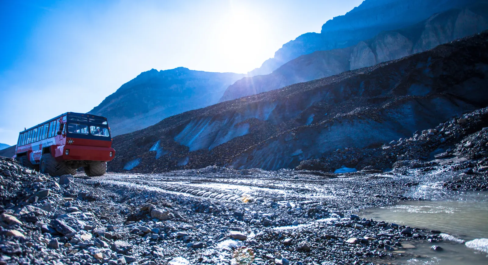 An Ice Explorer on the moraine track, backlit by sun over the Columbia Icefield