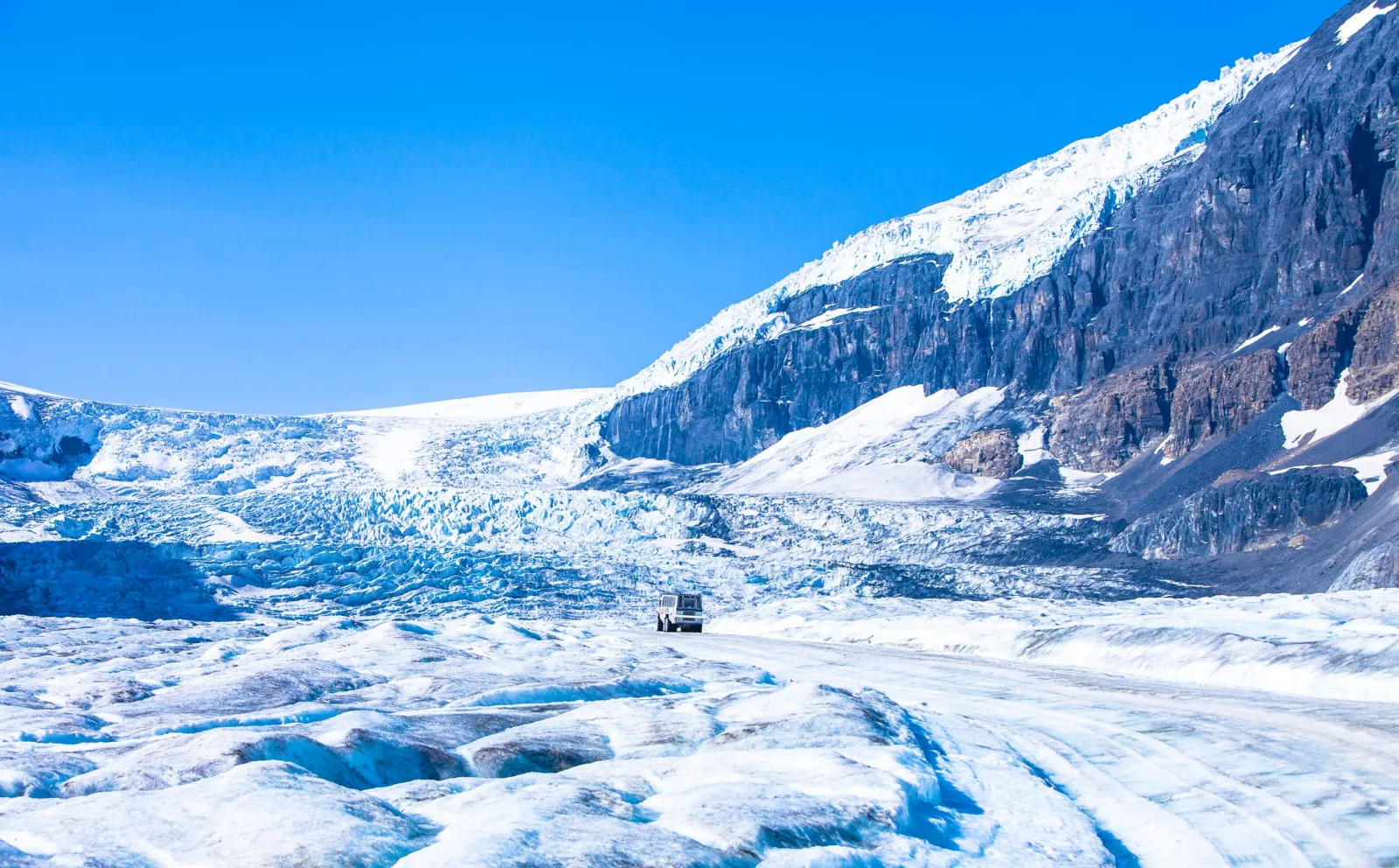 The Athabasca Glacier seen from the ice, a single Ice Explorer dwarfed by the icefall above