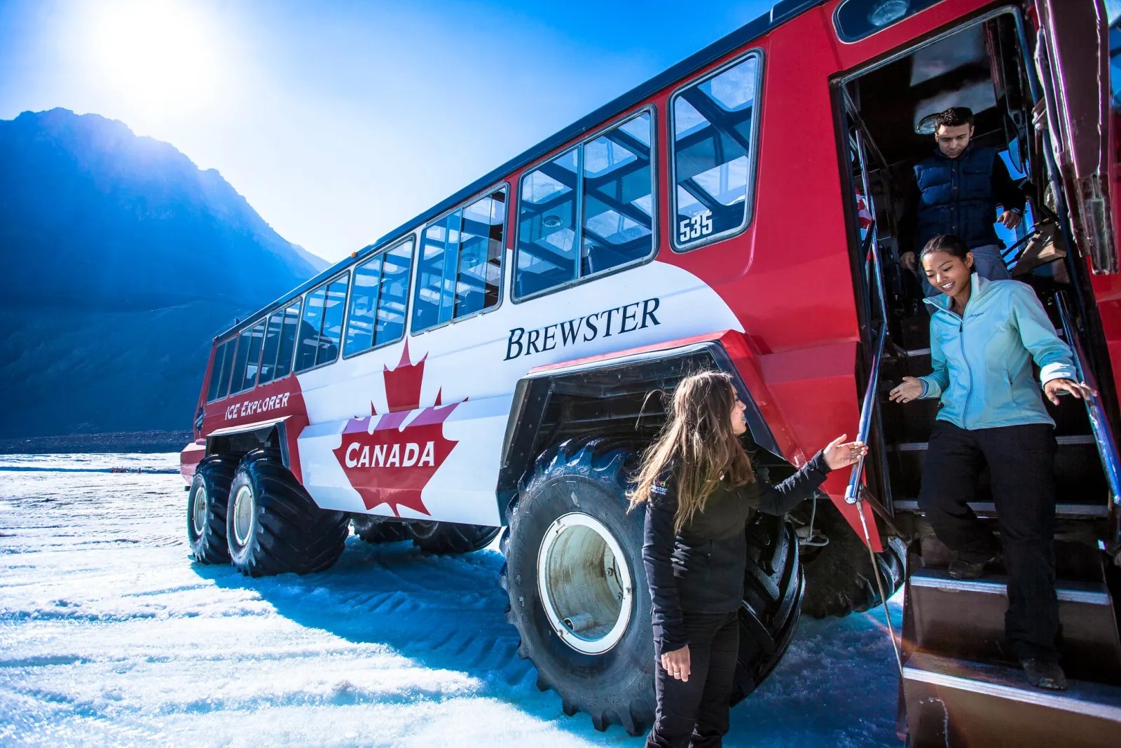 Passengers stepping down from an Ice Explorer onto the Athabasca Glacier in bright sun