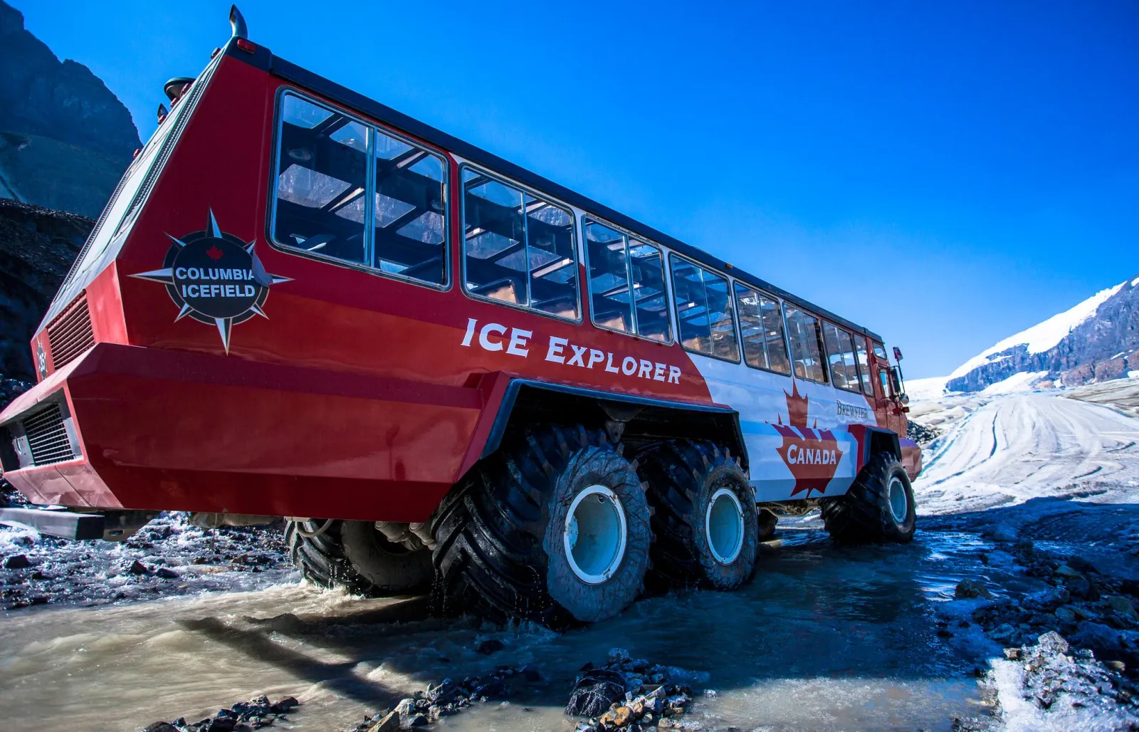 An Ice Explorer photographed from below, its oversized tires standing in glacial meltwater