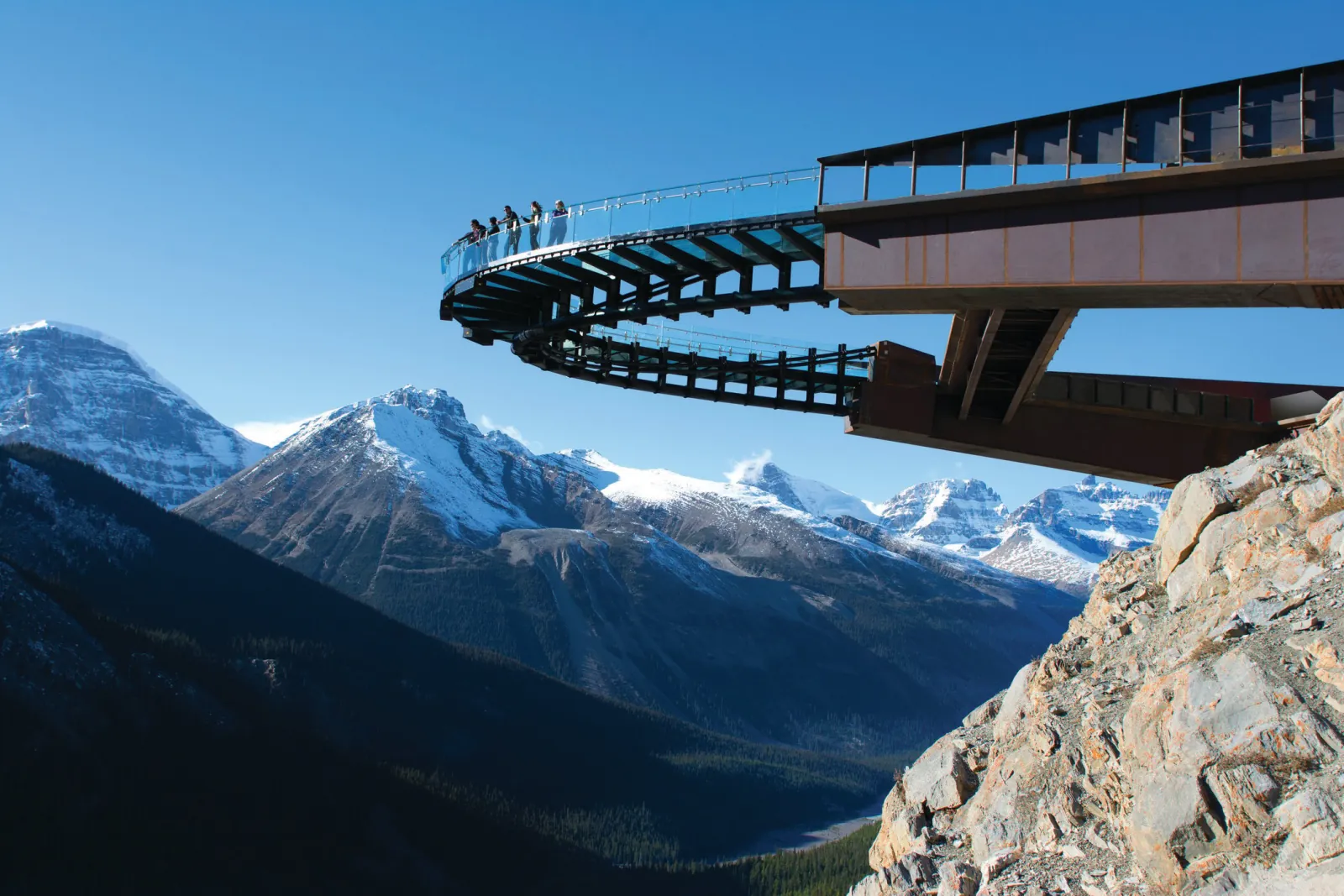 The Skywalk platform cantilevered from the cliff face, seen side-on above snow-covered Rockies peaks