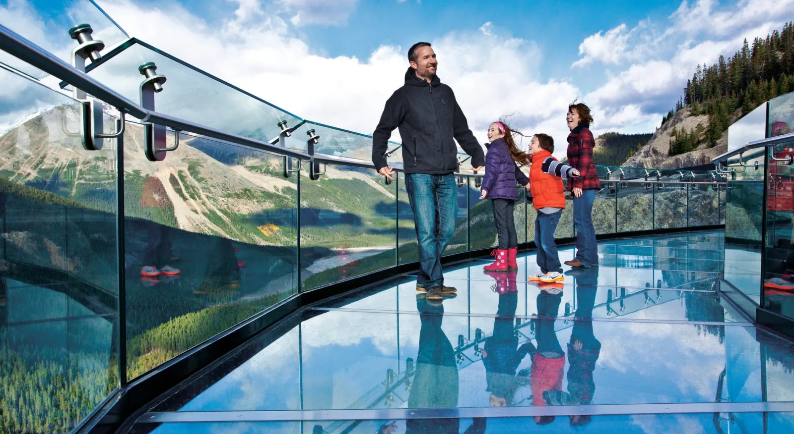 A family standing on the Skywalk's glass floor, their reflections in the panels beneath them