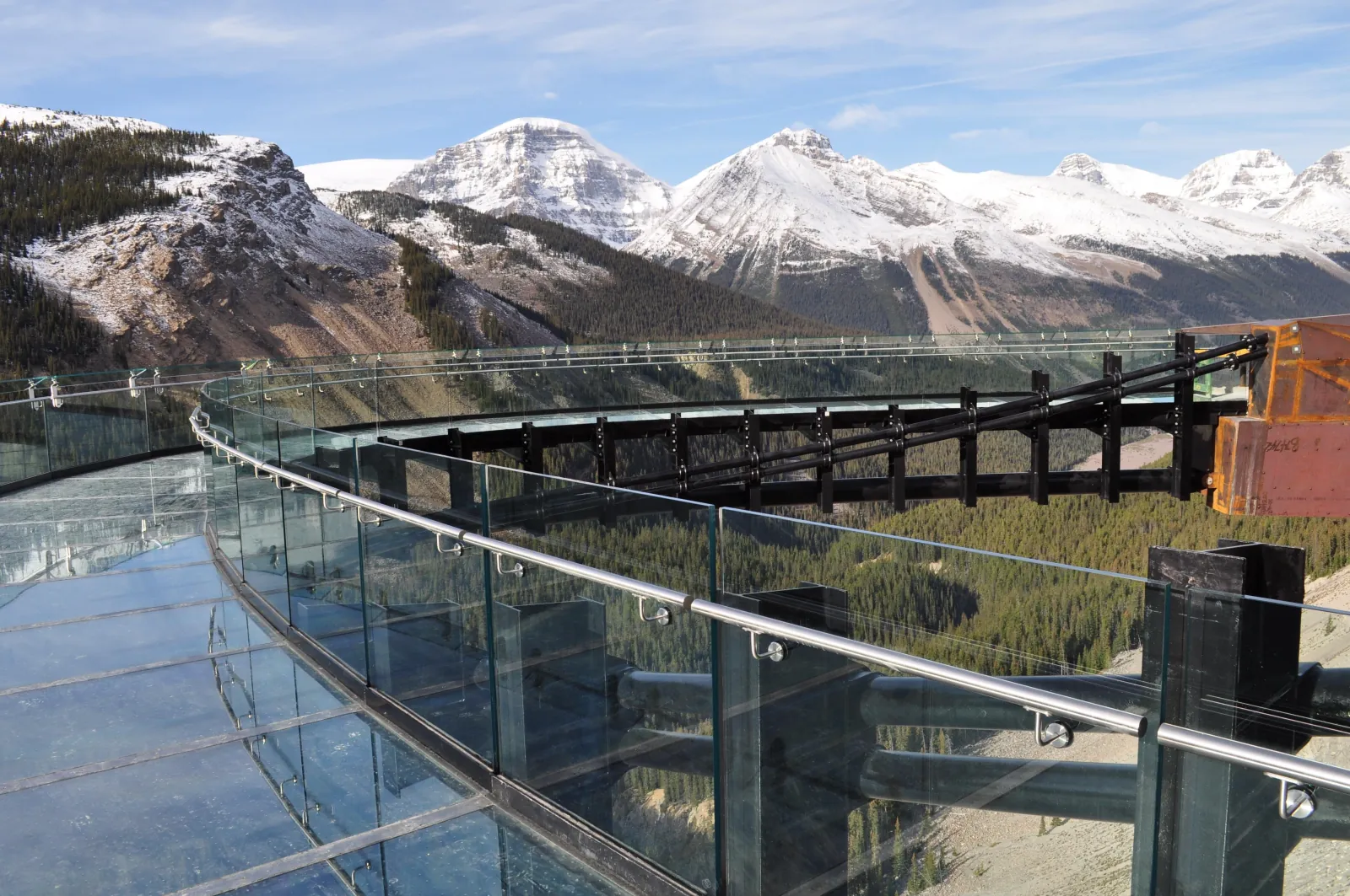 The curved glass walkway of the Skywalk with fresh snow on the surrounding peaks
