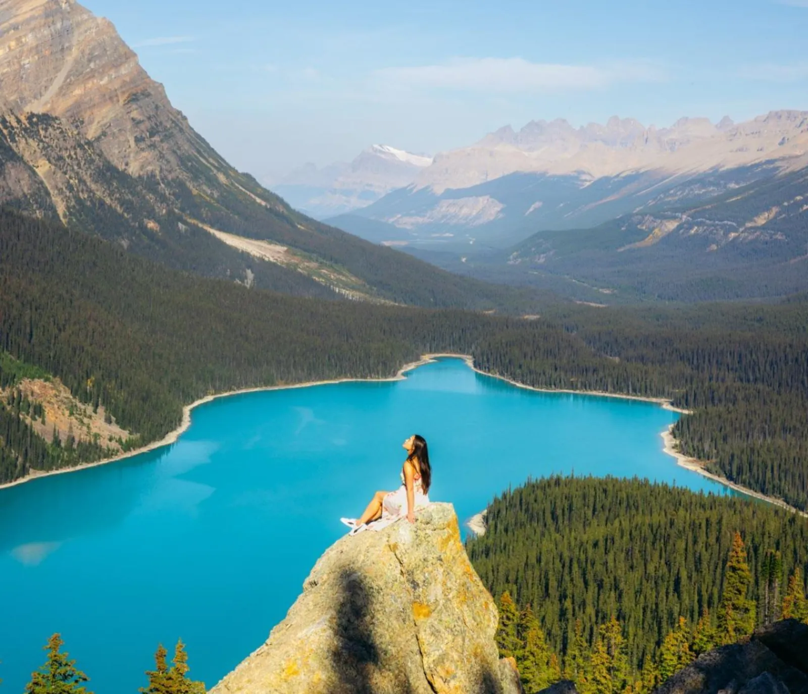 A visitor sitting on the rocky Peyto Lake overlook above the bright blue water