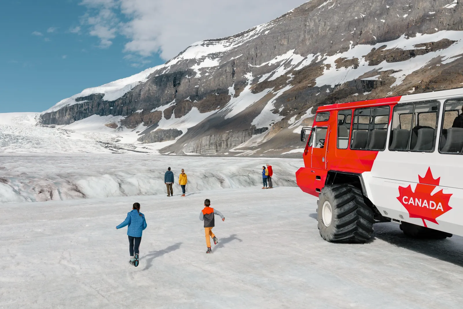 Children running across the Athabasca Glacier beside a red Ice Explorer, the icefall behind
