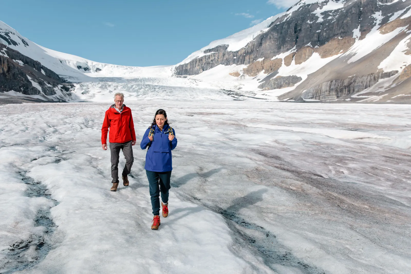 Two walkers crossing the Athabasca Glacier's ridged surface toward the icefall