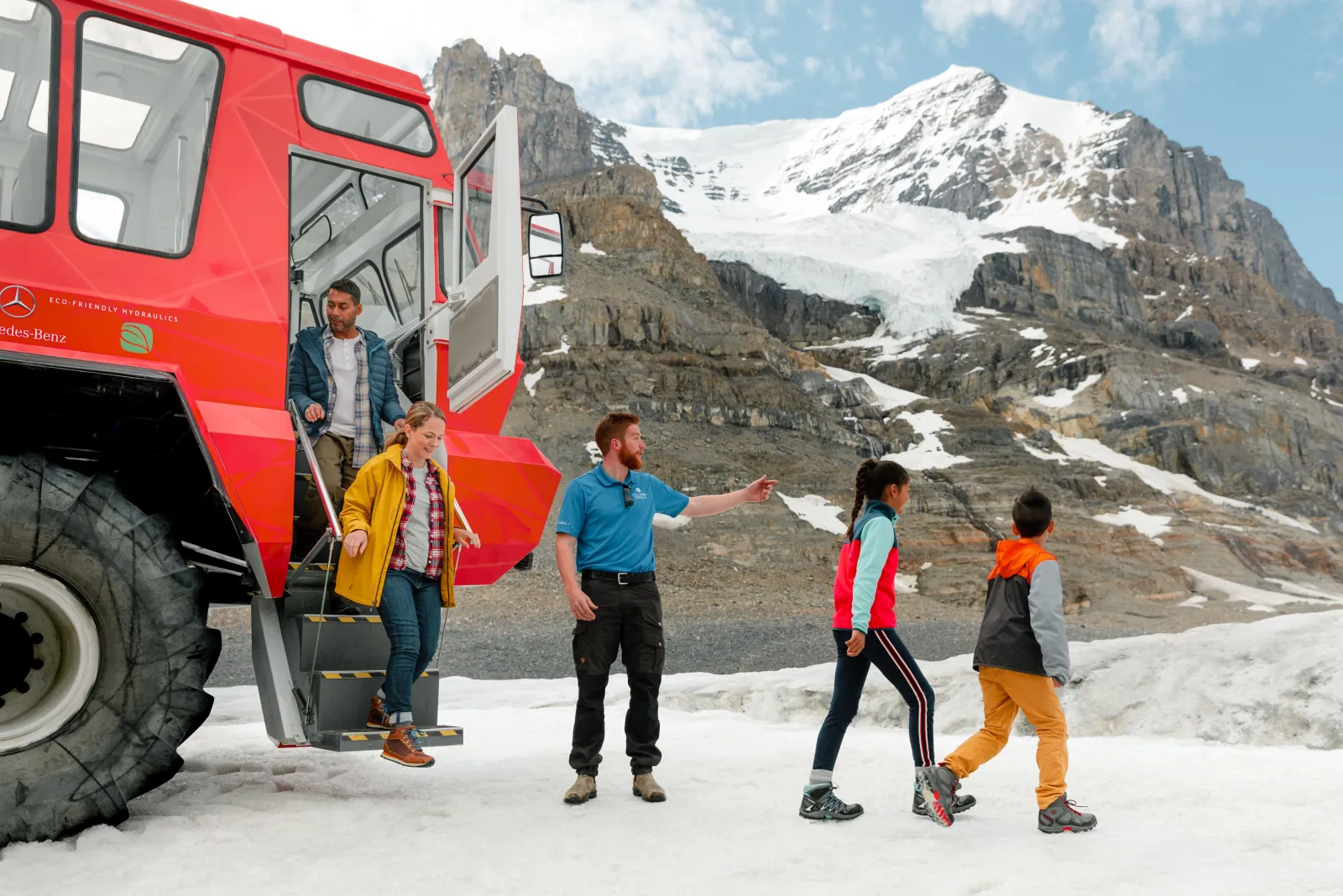 A guide directing a family off a red Ice Explorer onto the glacier below Mount Athabasca