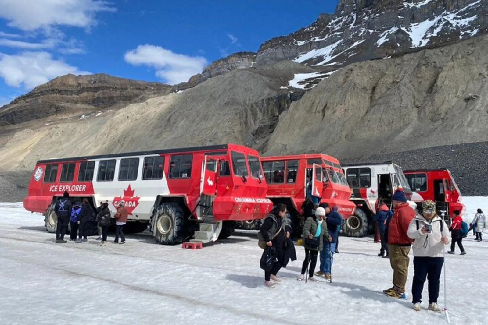 Three Ice Explorers lined up on the Athabasca Glacier as passengers step onto the ice