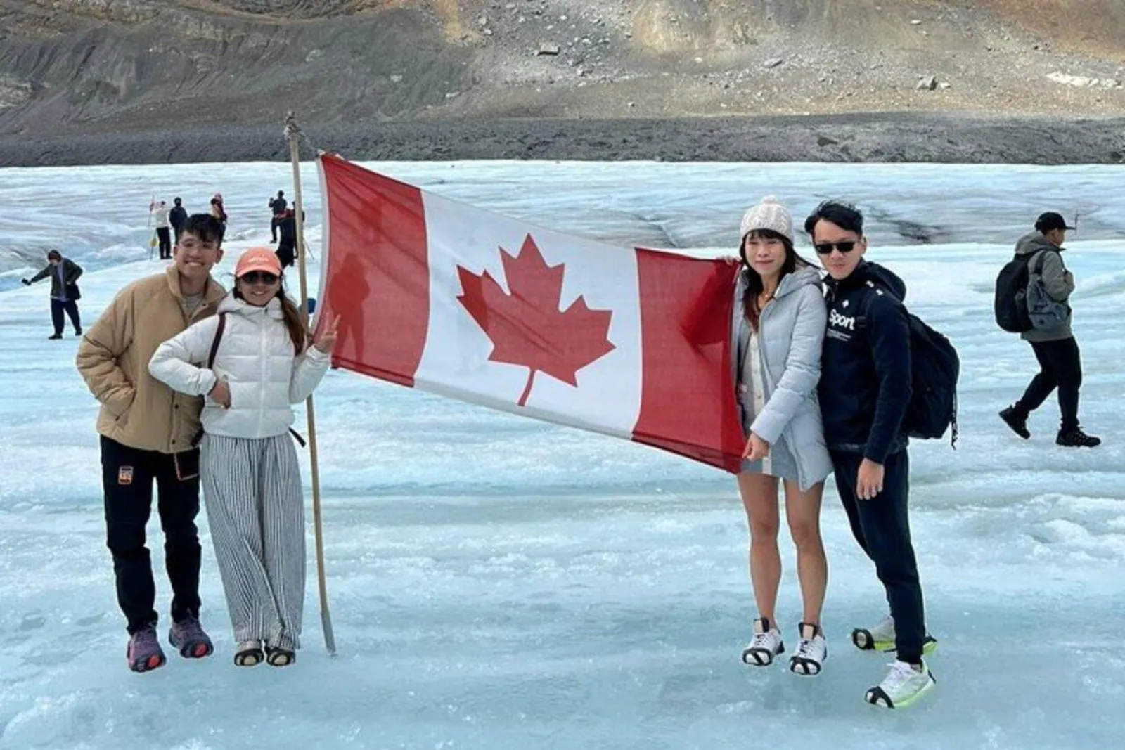 Visitors posing with a Canadian flag on the blue ice of the Athabasca Glacier