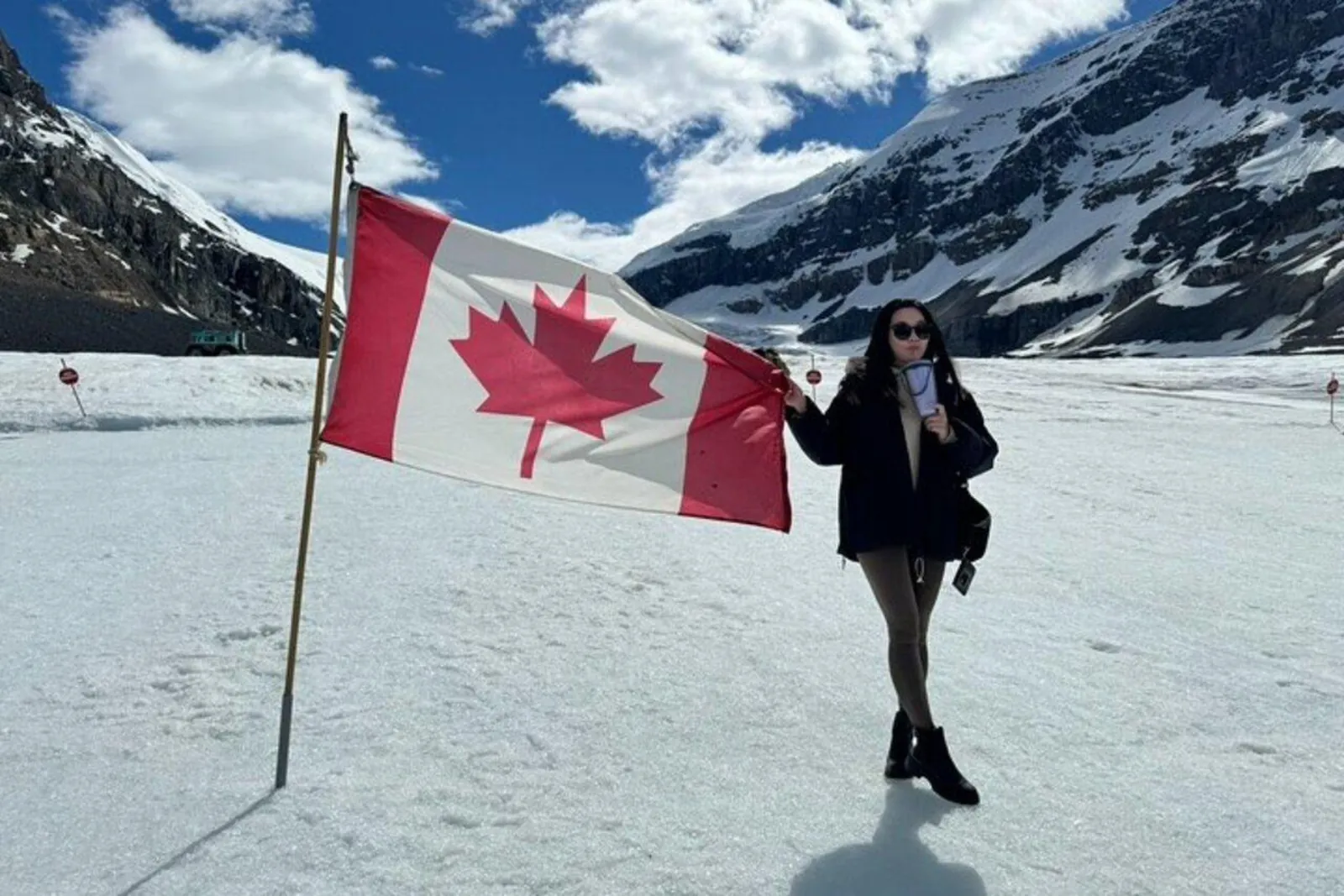 A visitor beside the Canadian flag planted on the Athabasca Glacier, the icefall behind