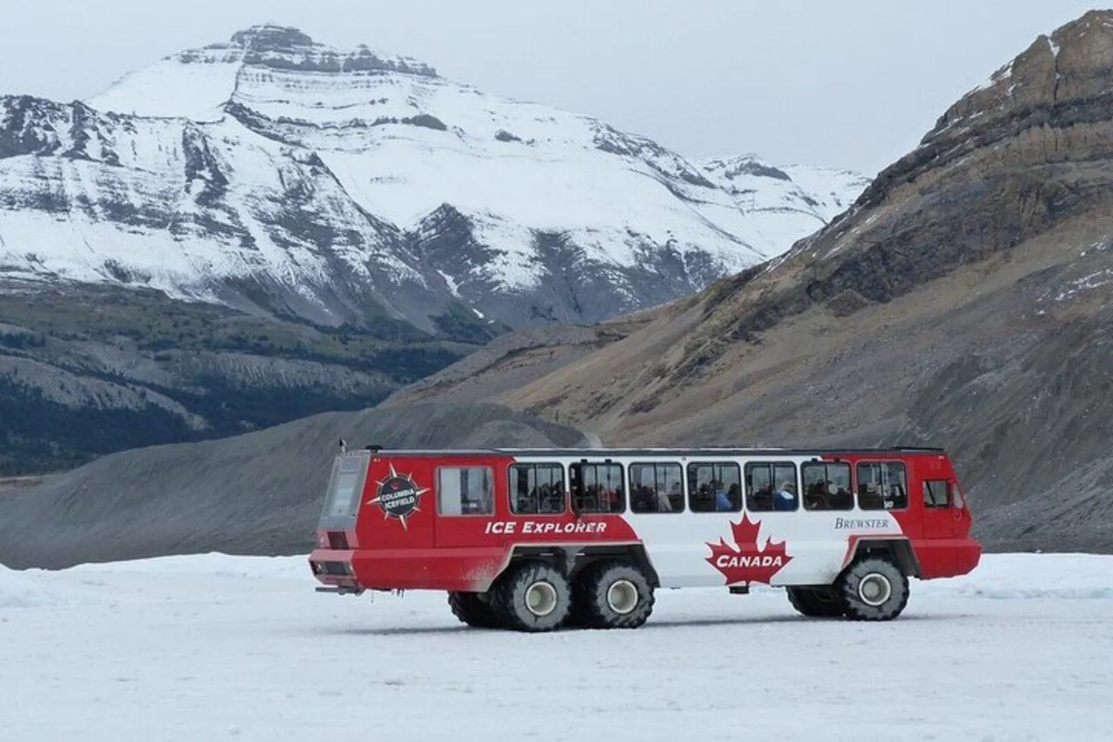 A red Ice Explorer crossing the Athabasca Glacier below a snow-covered summit